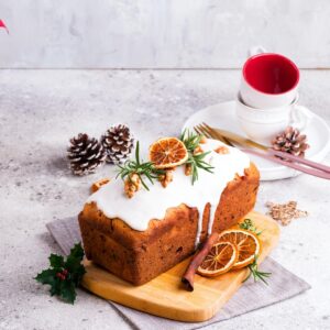 Fruit loaf cake dusted with icing, nuts and dry orange on stone background. Christmas and Winter