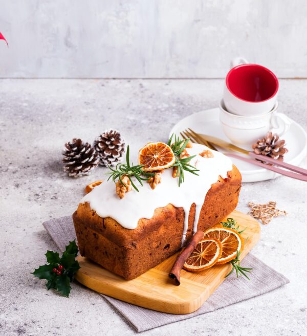 Fruit loaf cake dusted with icing, nuts and dry orange on stone background. Christmas and Winter